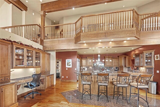 187 Fox Ridge Dr, Evergreen, CO 80439 - kitchen with wall chimney exhaust hood, a high ceiling, a breakfast bar area, decorative backsplash, and light wood-type flooring