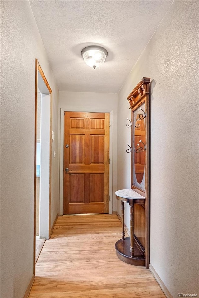 corridor with a textured ceiling and light hardwood / wood-style floors