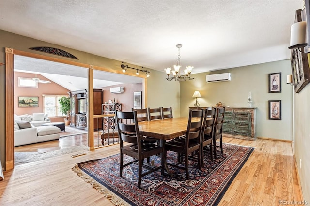 dining space with an inviting chandelier, an AC wall unit, a textured ceiling, and light wood-type flooring