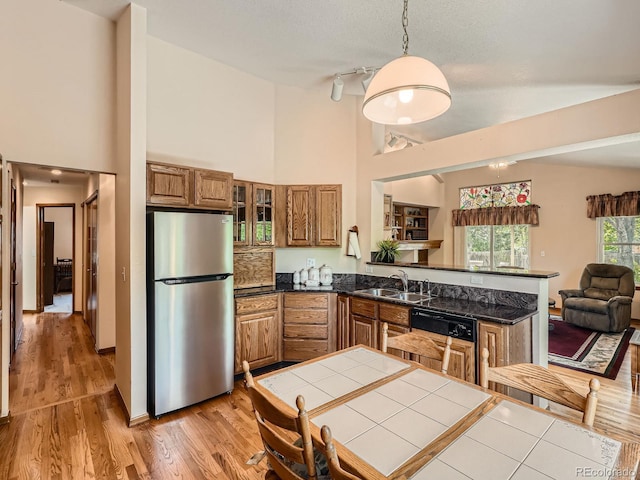 kitchen with freestanding refrigerator, a sink, brown cabinetry, a high ceiling, and a peninsula