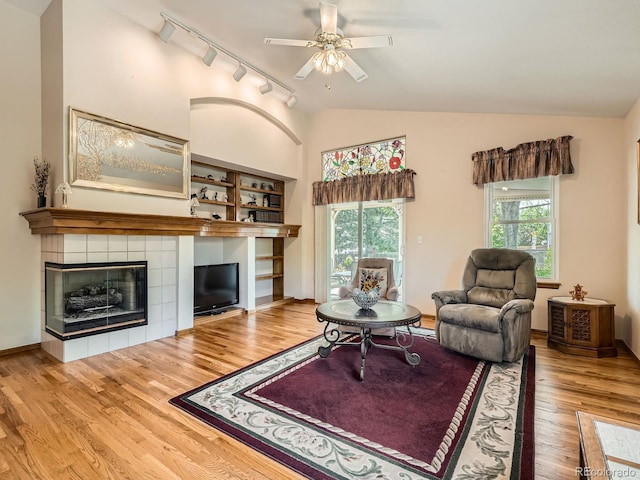 living room featuring track lighting, lofted ceiling, wood finished floors, ceiling fan, and a tiled fireplace