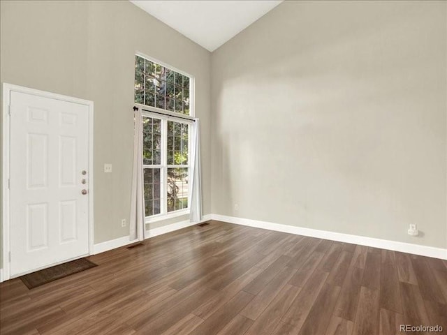 spare room with dark wood-style floors, baseboards, and high vaulted ceiling