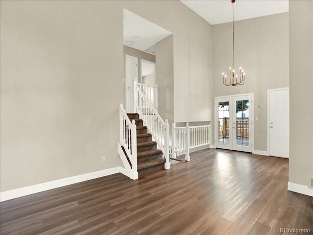 foyer with baseboards, dark wood-style floors, a towering ceiling, a chandelier, and stairway