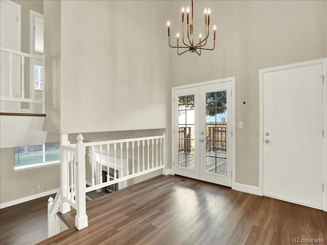 foyer featuring french doors, wood finished floors, baseboards, a towering ceiling, and a chandelier