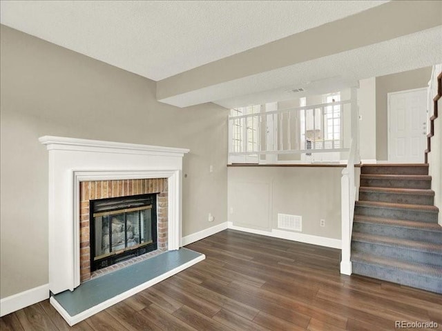 unfurnished living room with baseboards, wood finished floors, stairway, a brick fireplace, and a textured ceiling