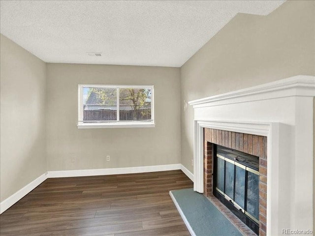 unfurnished living room with a brick fireplace, wood finished floors, a textured ceiling, and baseboards