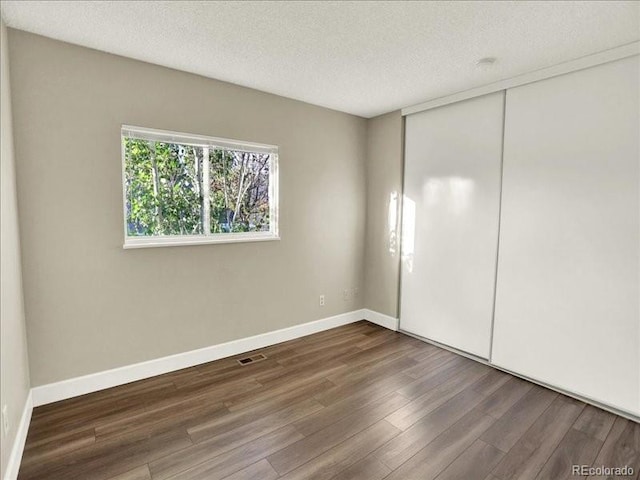 unfurnished bedroom with wood finished floors, a textured ceiling, a closet, and baseboards