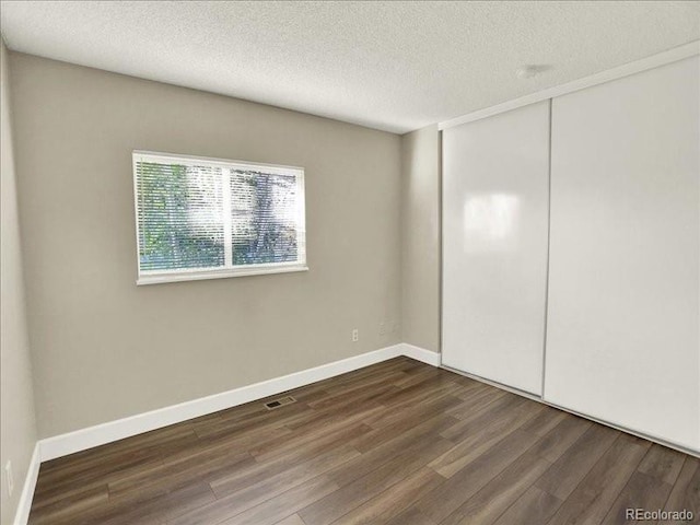 unfurnished bedroom with dark wood finished floors, a closet, a textured ceiling, and baseboards