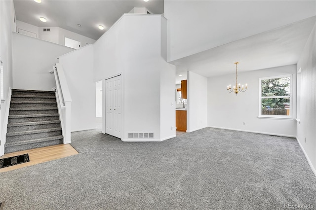 unfurnished living room with an inviting chandelier, carpet floors, stairs, and visible vents