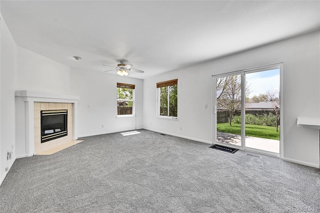 unfurnished living room featuring carpet flooring, ceiling fan, a tiled fireplace, and baseboards