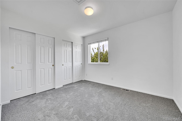 unfurnished bedroom featuring two closets, baseboards, visible vents, and carpet