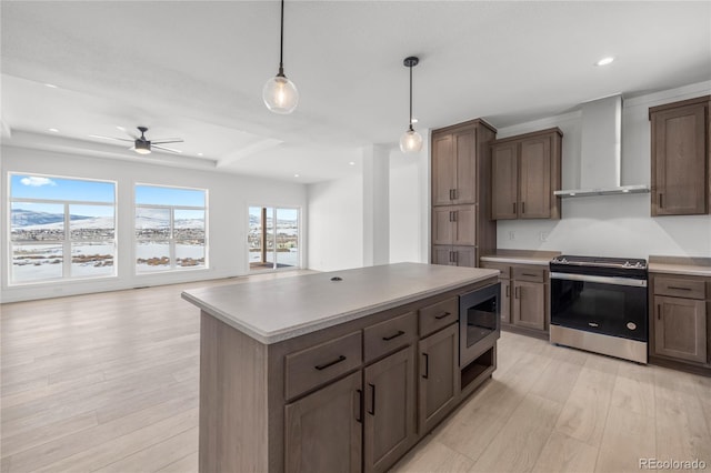 kitchen with a center island, stainless steel appliances, light countertops, wall chimney range hood, and pendant lighting