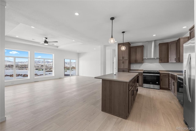 kitchen with a center island, pendant lighting, appliances with stainless steel finishes, open floor plan, and wall chimney range hood