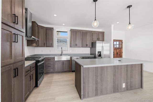 kitchen with light countertops, hanging light fixtures, appliances with stainless steel finishes, a kitchen island, and wall chimney exhaust hood