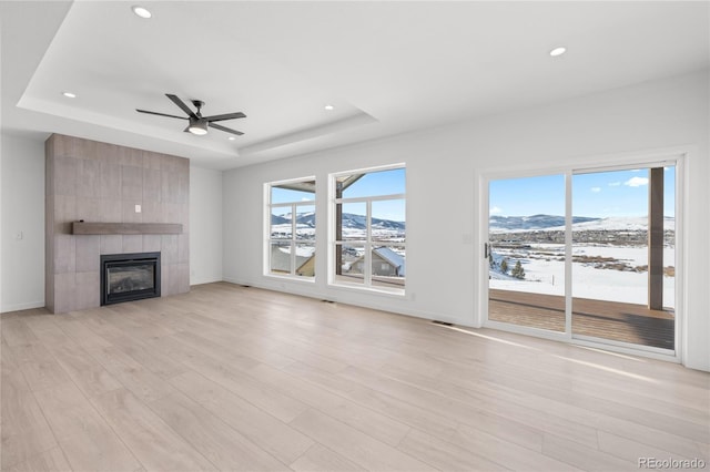 unfurnished living room featuring light wood finished floors, recessed lighting, a raised ceiling, a mountain view, and a tile fireplace