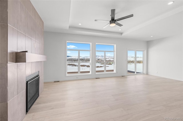 unfurnished living room with light wood finished floors, a tray ceiling, a fireplace, and recessed lighting