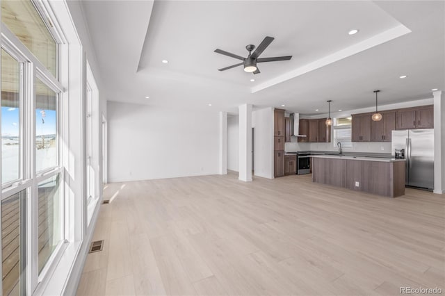 unfurnished living room with a tray ceiling, light wood-type flooring, visible vents, and a ceiling fan