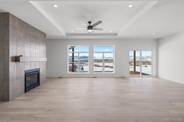 unfurnished living room featuring light wood-style floors, ceiling fan, a tray ceiling, and a tile fireplace