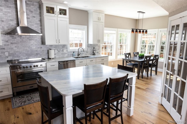 kitchen featuring white cabinets, stainless steel appliances, sink, and wall chimney range hood