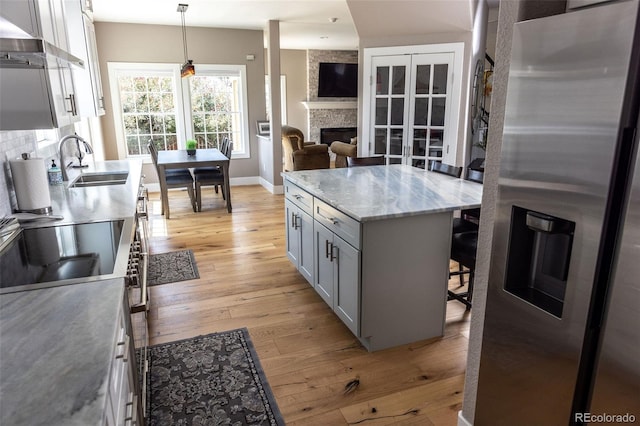 kitchen featuring pendant lighting, sink, wall chimney range hood, stainless steel refrigerator with ice dispenser, and light hardwood / wood-style floors