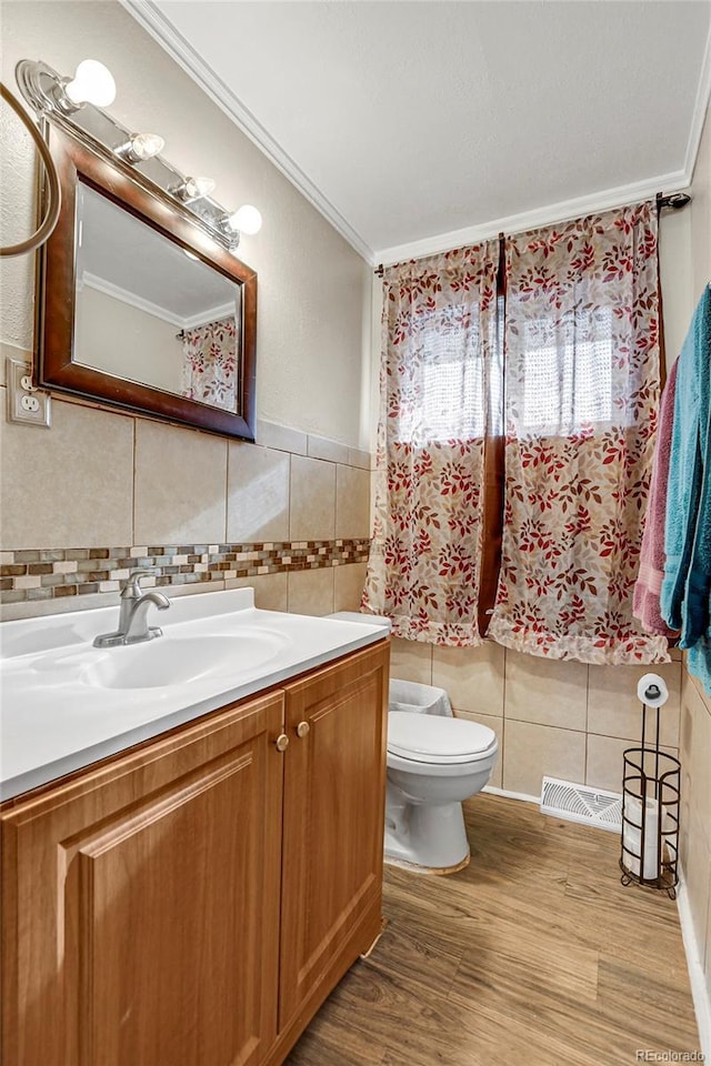 bathroom featuring toilet, hardwood / wood-style flooring, tile walls, ornamental molding, and vanity