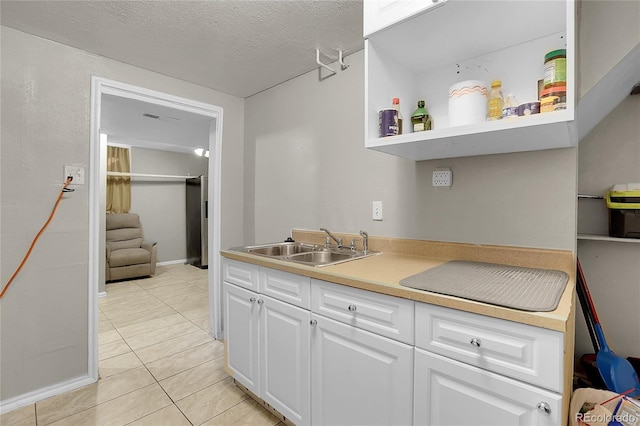 kitchen featuring sink, light tile patterned floors, white cabinetry, and a textured ceiling