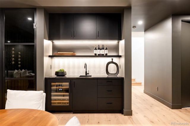 bar featuring sink, beverage cooler, and light hardwood / wood-style flooring