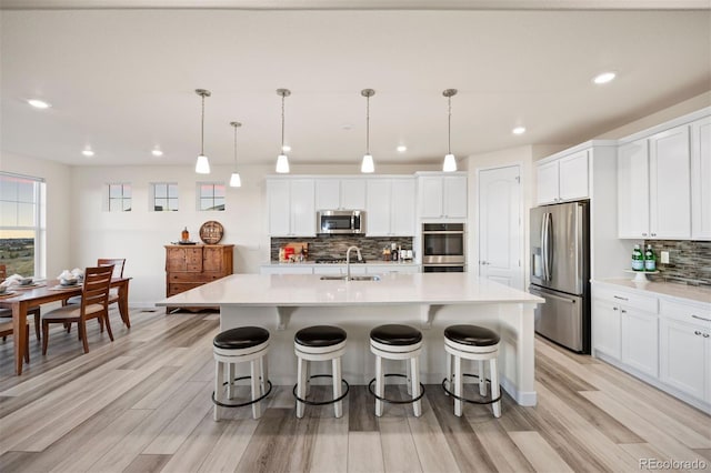 kitchen with appliances with stainless steel finishes, light countertops, a sink, decorative backsplash, and a breakfast bar area