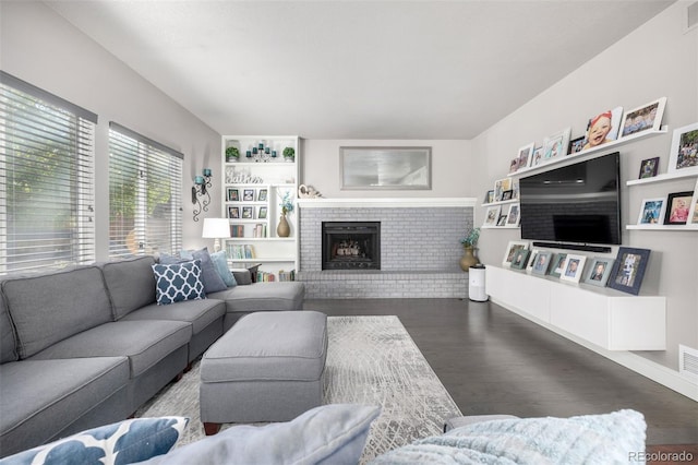 living area with visible vents, a brick fireplace, wood finished floors, baseboards, and built in shelves