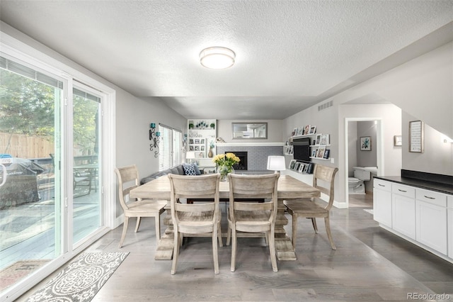 dining area featuring a fireplace, a textured ceiling, baseboards, wood finished floors, and visible vents