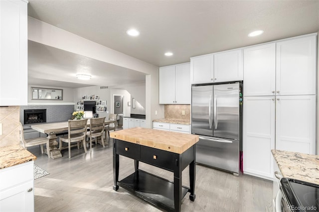 kitchen featuring light wood-style floors, a fireplace with raised hearth, white cabinets, tasteful backsplash, and appliances with stainless steel finishes