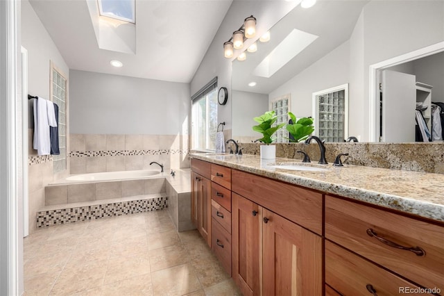 bathroom with double vanity, a sink, a bath, and vaulted ceiling with skylight
