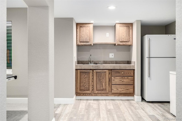 kitchen with freestanding refrigerator, brown cabinetry, a sink, and light wood-style flooring