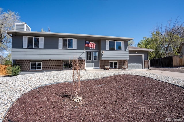 split foyer home featuring concrete driveway, a chimney, an attached garage, fence, and brick siding