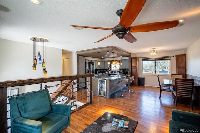living area featuring light wood finished floors, beverage cooler, a textured ceiling, and ceiling fan