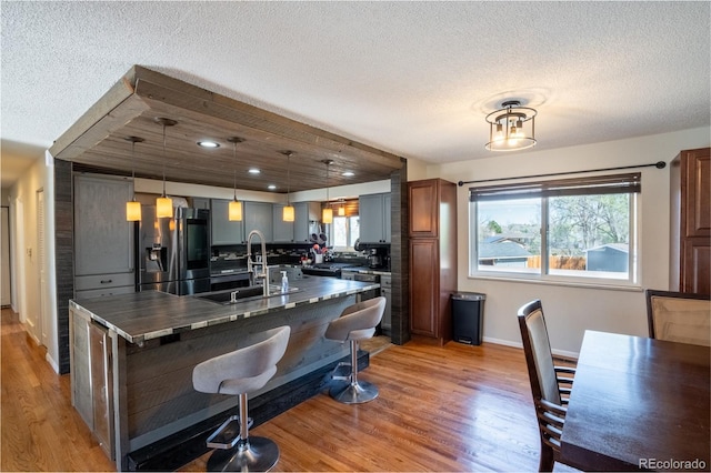 kitchen featuring light wood finished floors, a sink, a textured ceiling, dark countertops, and stainless steel fridge with ice dispenser