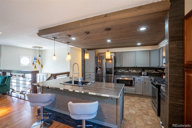 kitchen with a sink, a kitchen bar, gray cabinets, an island with sink, and appliances with stainless steel finishes