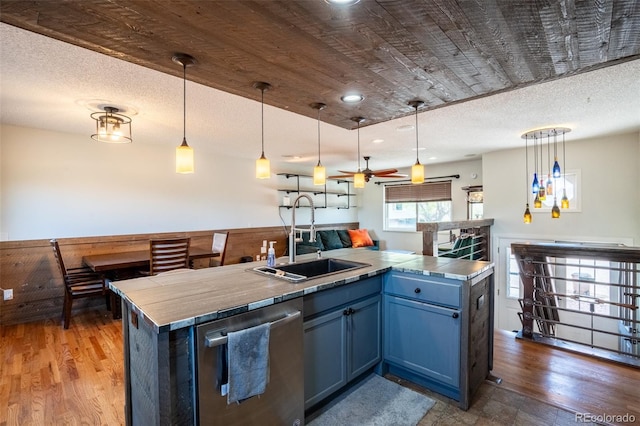 kitchen featuring stainless steel dishwasher, hanging light fixtures, wood finished floors, a sink, and blue cabinetry
