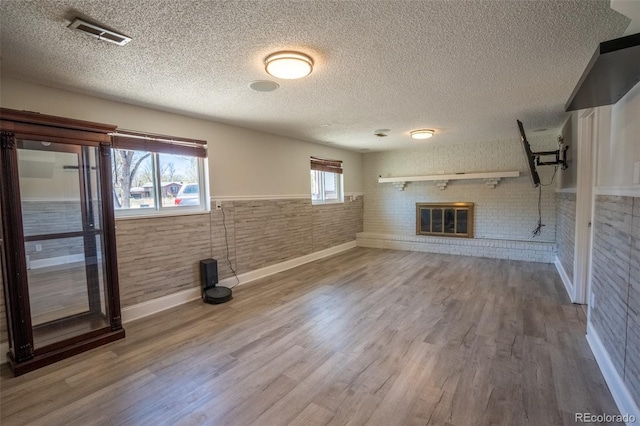 basement featuring a textured ceiling, baseboards, visible vents, wood finished floors, and a fireplace