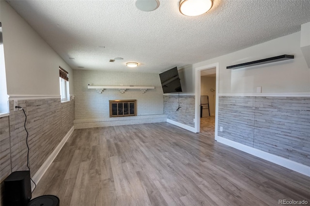 unfurnished living room featuring a wainscoted wall, wood finished floors, baseboards, a fireplace, and a textured ceiling