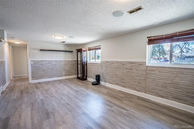 below grade area with visible vents, a textured ceiling, baseboards, and wainscoting