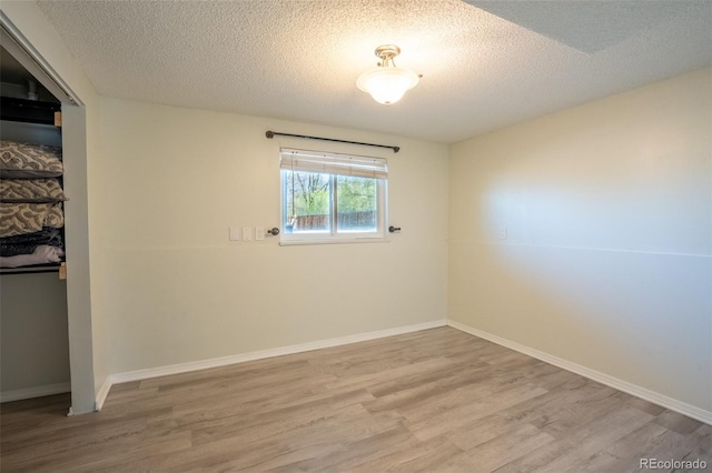 spare room featuring baseboards, wood finished floors, and a textured ceiling
