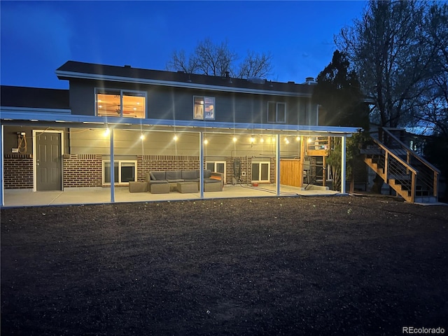 back of house at twilight featuring an outdoor living space, stairway, and a patio
