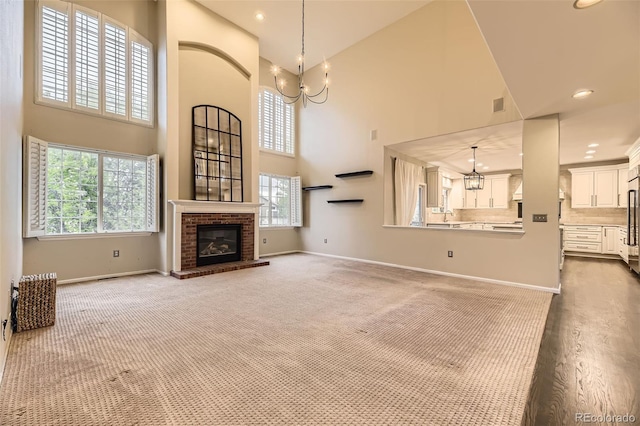 unfurnished living room with a chandelier, a high ceiling, light carpet, healthy amount of natural light, and baseboards
