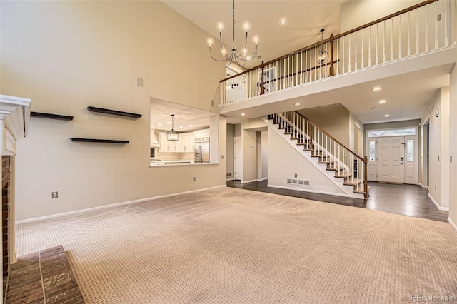 unfurnished living room featuring a chandelier, dark carpet, baseboards, stairway, and a towering ceiling