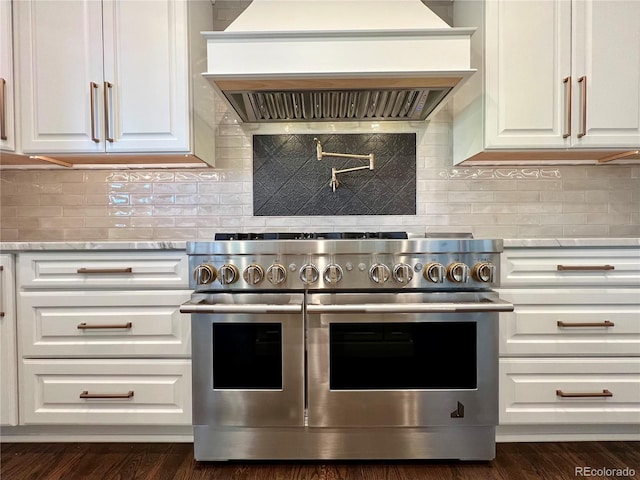 kitchen featuring double oven range, custom range hood, white cabinetry, and backsplash