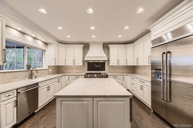 kitchen with stainless steel appliances, custom range hood, white cabinets, a sink, and recessed lighting