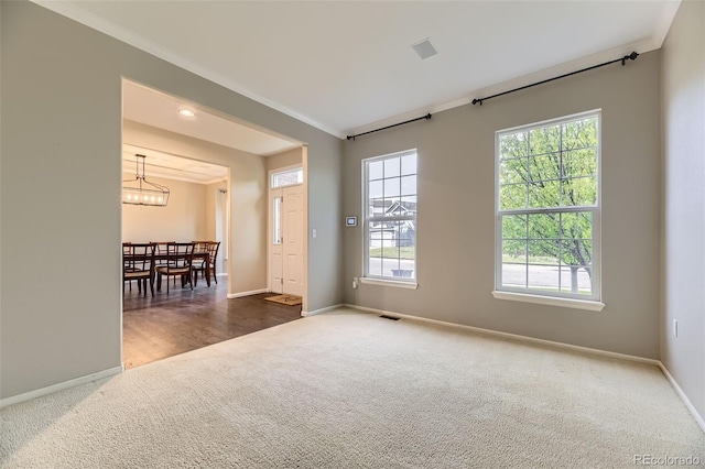 carpeted spare room with crown molding, baseboards, and a chandelier