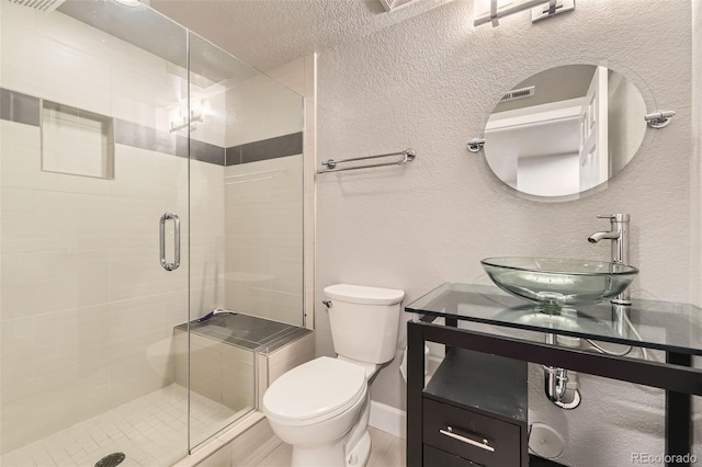 bathroom with toilet, a shower stall, vanity, a textured wall, and baseboards