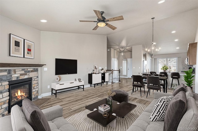 living room with ceiling fan with notable chandelier, light hardwood / wood-style floors, a stone fireplace, and lofted ceiling